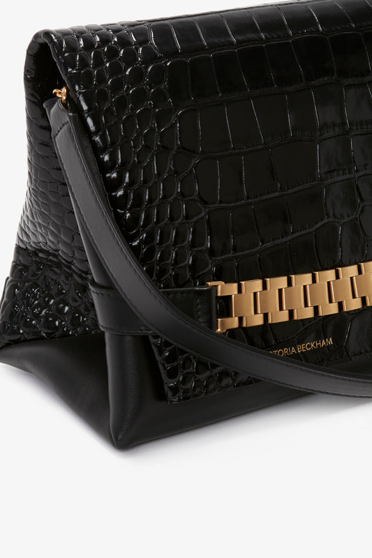 Close-up of a black, croc-embossed Chain Pouch Bag With Strap In Black Croc-Effect Leather with a gold chain detail. The brand name Victoria Beckham is visible on the front.