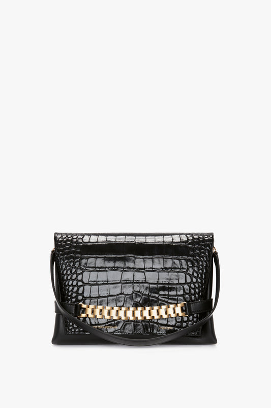 A Chain Pouch Bag With Strap In Black Croc-Effect Leather, reminiscent of Victoria Beckham's sophisticated style, features a gold chain detail on the front and a shoulder strap. It’s beautifully showcased against a plain white background.
