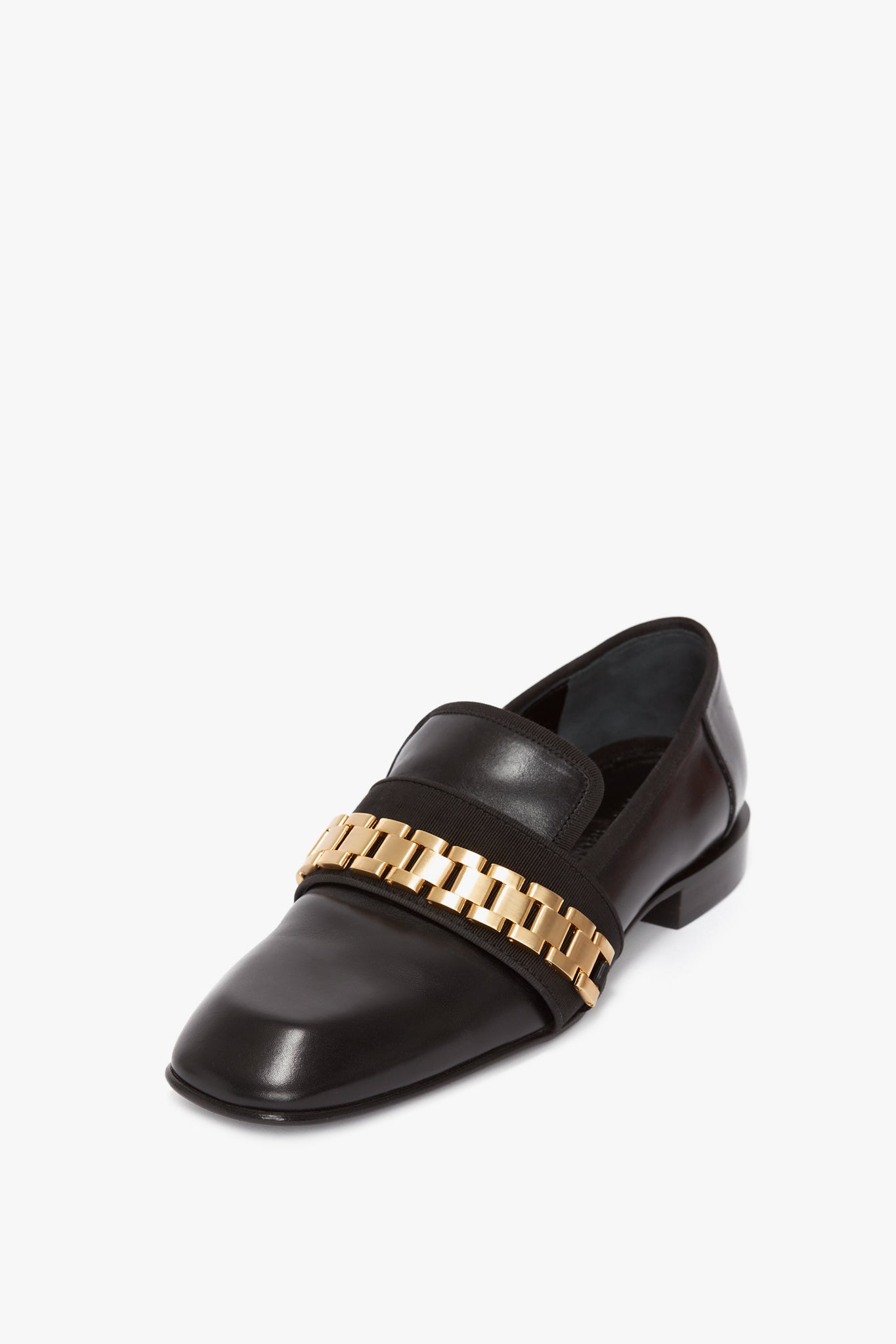 Introducing the Mila Chain Loafer In Black by Victoria Beckham: a black patent leather loafer with a square toe design, featuring a gold chain detail across the top, balancing both masculine and feminine energy on a plain white background.