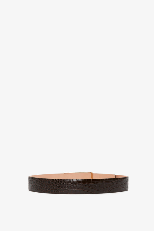 A dark brown Jumbo Frame Belt In Chocolate Croc-Effect Leather crafted from croc-effect leather, featuring a gold rectangular buckle, displayed against a white background. This piece by Victoria Beckham combines contemporary styling with timeless elegance.
