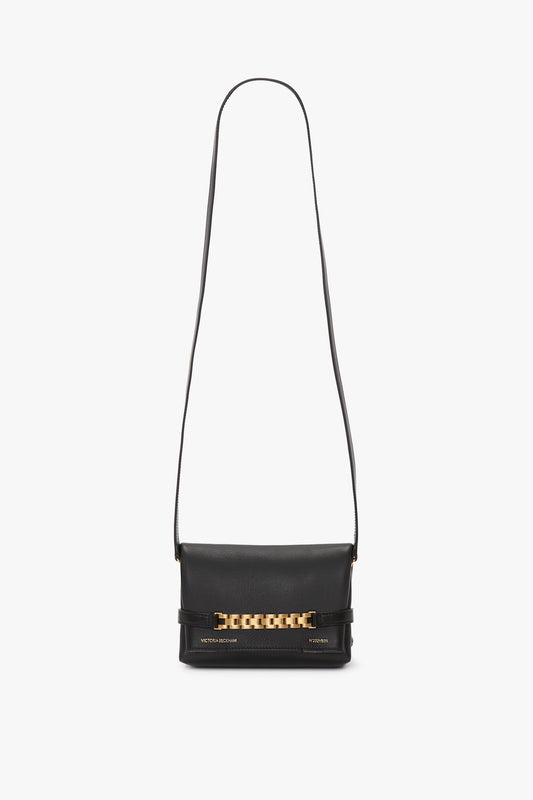 Mini Chain Pouch Bag With Long Strap In Black Leather by Victoria Beckham featuring a long strap, gold-tone watch strap detail on the front flap, and small brand name embossing at the bottom.