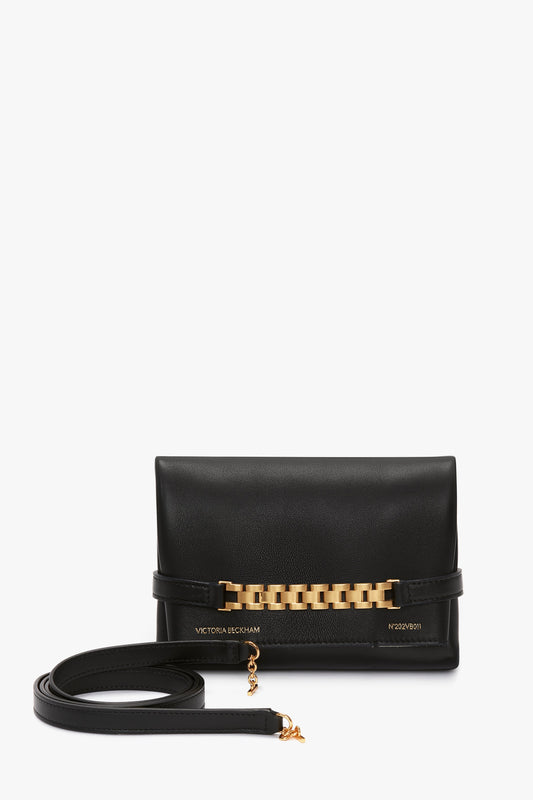 A Victoria Beckham Mini Chain Pouch Bag With Long Strap In Black Leather with a gold-tone watch strap detail on the front and a slim strap placed beside it.