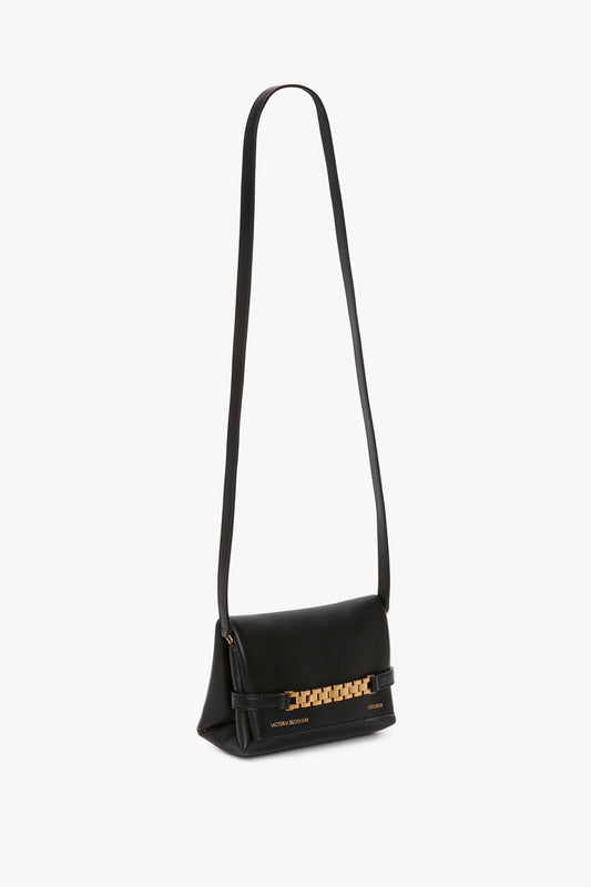 A black leather shoulder bag with a long strap, featuring a gold chain detail and the brand's name embossed in gold at the bottom. The Mini Chain Pouch Bag With Long Strap In Black Leather by Victoria Beckham adds a touch of elegance with its versatile design.