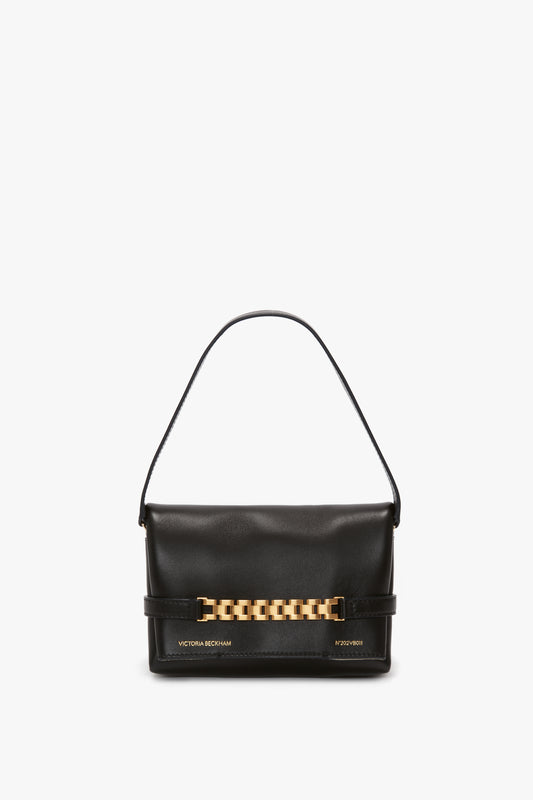 A classic black leather handbag with a short strap, enhanced by gold-tone hardware and metallic writing on the bottom, also known as the Victoria Beckham Mini Chain Pouch Bag In Black Leather.