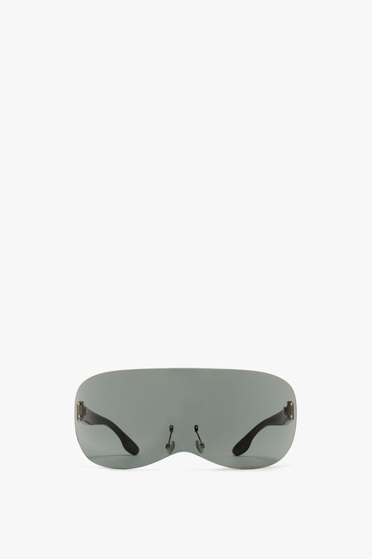 A pair of futuristic, frameless Victoria Beckham Oversized Shield Sunglasses with grey smoke nylon lenses and black temple arms, isolated on a white background.