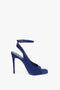 The Dawn Sandal in Night Blue Suede by Victoria Beckham, a single blue high-heeled sandal with an ankle strap and open toe on a plain white background, offers a versatile and sophisticated finishing touch to any outfit.